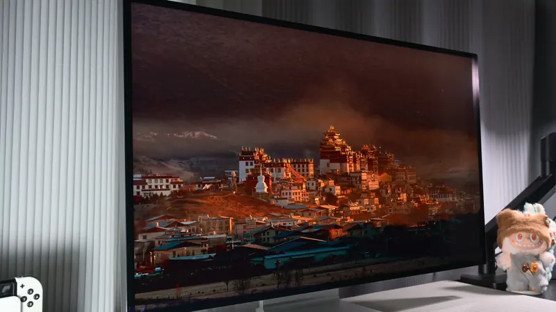 Three-quarter view of the Kuycon P32K monitor in a dark room, showing a monastery with golden roofs under a twilight sky